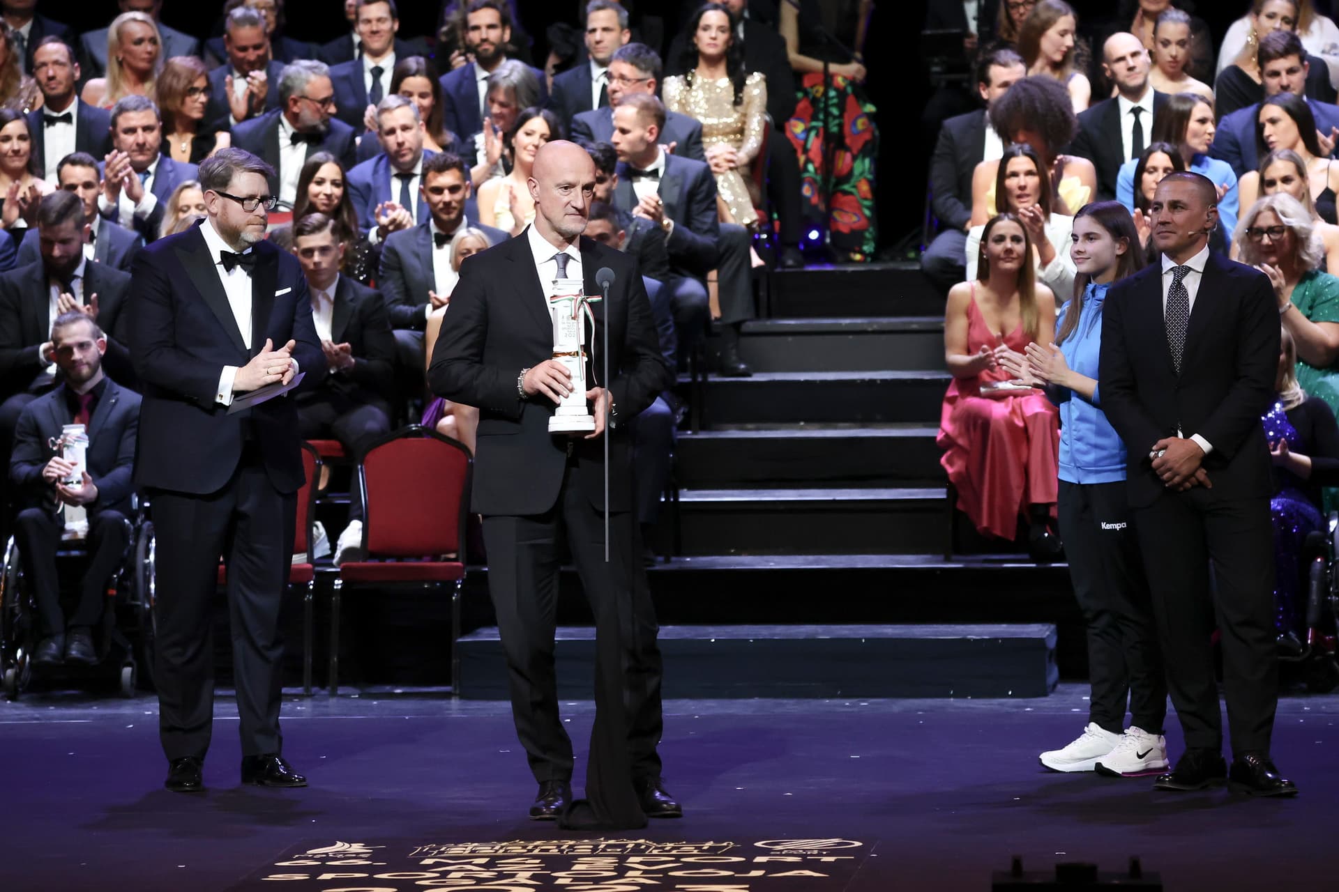 Marco Rossi, a labdarúgó-válogatott szövetségi kapitánya (k) kapta az Év edzője díjat az M4 Sport-Az Év Sportolója Gálán a Magyar Állami Operaházban 2024. január 8-án. Balról Szöllősi György, a Magyar Sportújságírók Szövetségének elnöke, a Nemzeti Sport főszerkesztője, jobbról Fabio Cannavaro korábbi aranylabdás olasz labdarúgó